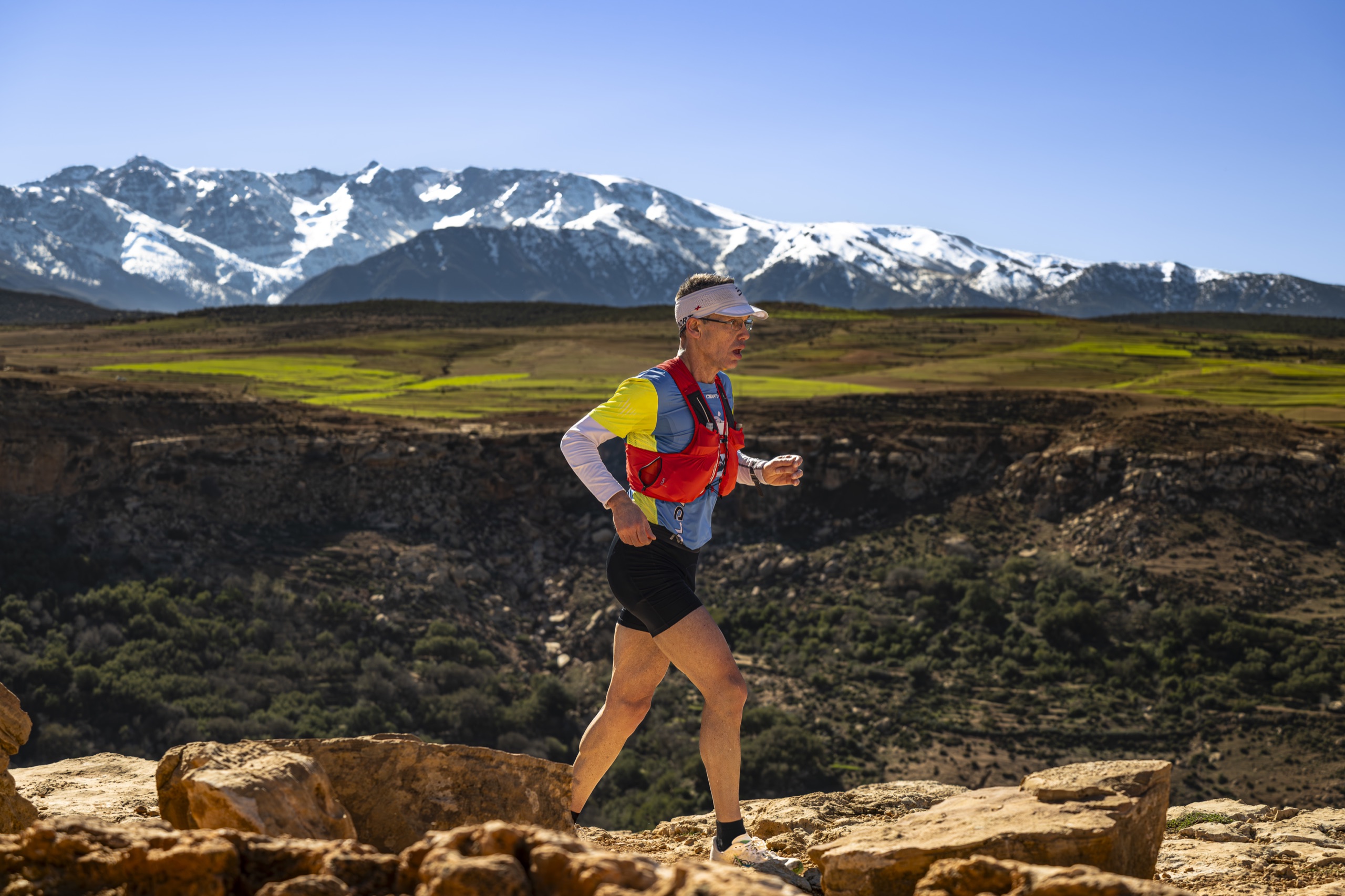 Coureur du Trail Takerkoust devant les sommets enneigés du Haut Atlas