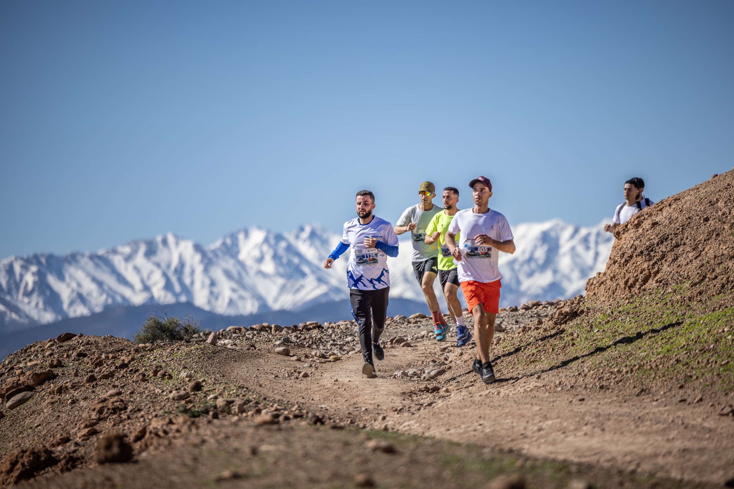 Coureurs du Trail Takerkoust face aux sommets enneigés du Haut Atlas